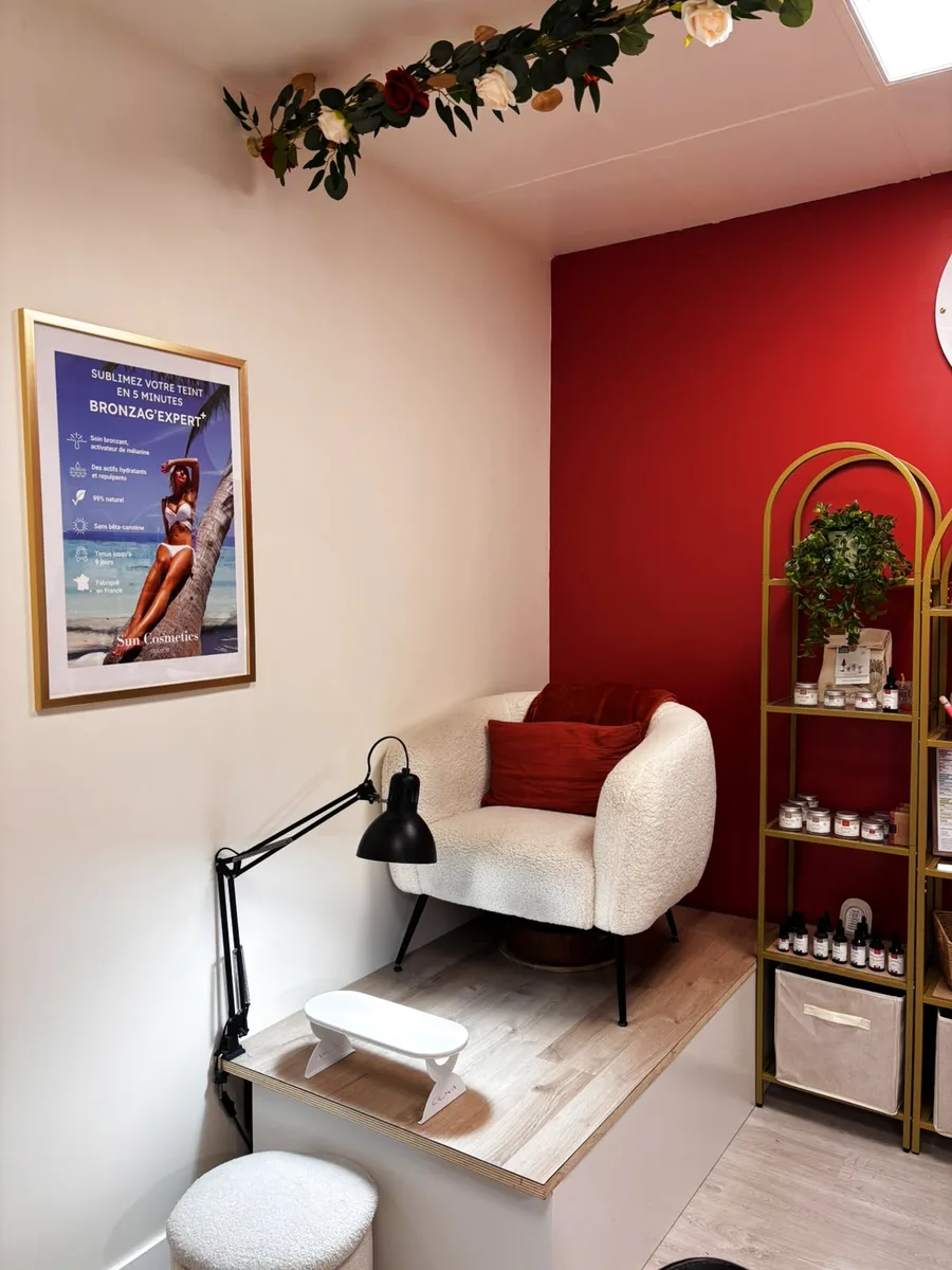 La cabine de l’institut : fauteuil blanc, repose-pieds, étagères dorées et guirlande de fleurs